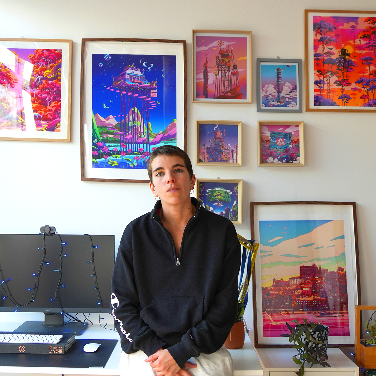 camila_illustration sitting in front of a wall with colorful, framed artwork of her prints.