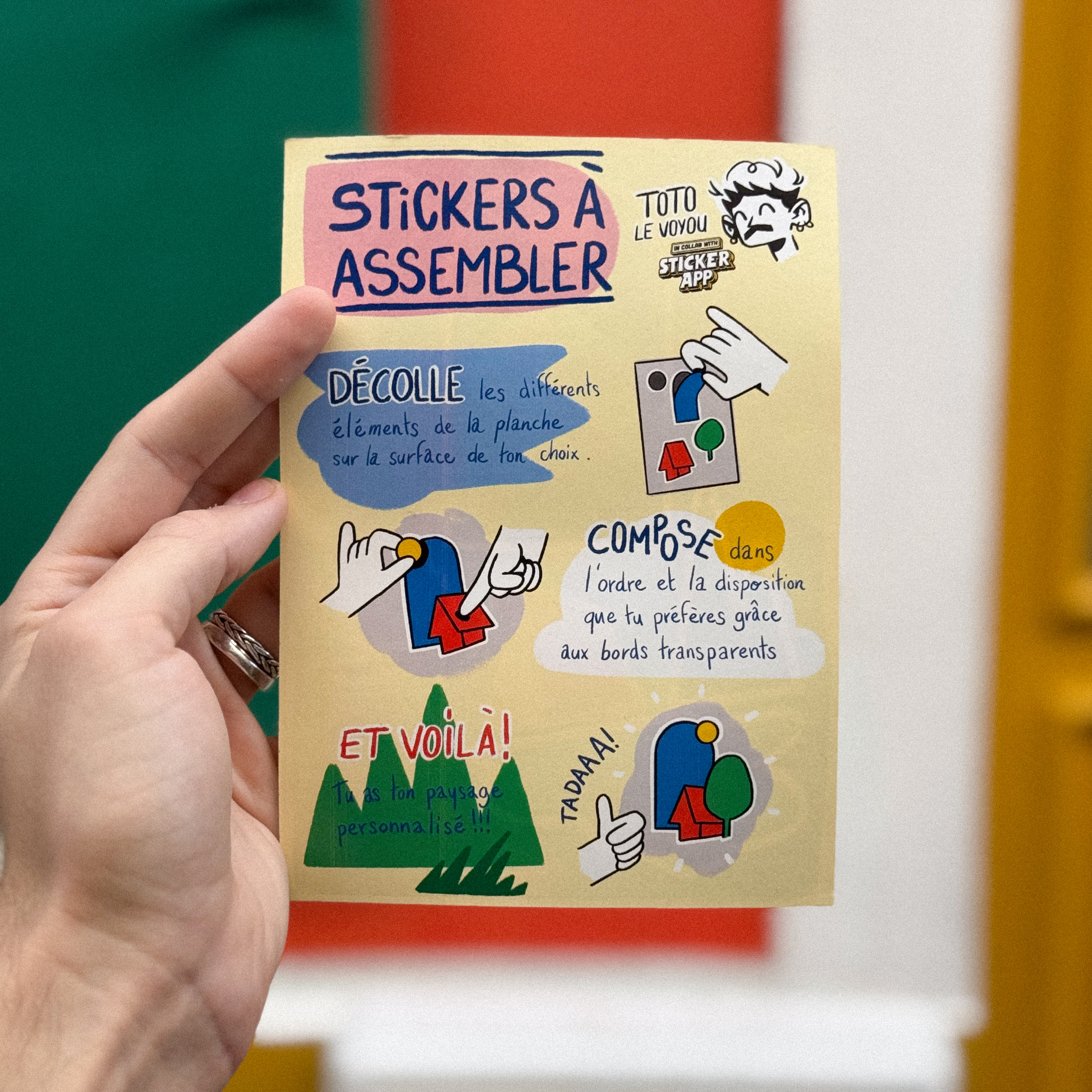 Hand holding a colorful sticker sheet with instructions for assembling and personalizing stickers on a surface.