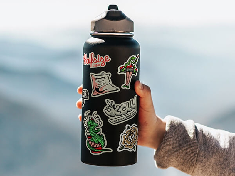 A hand holding a black water bottle with seven stickers